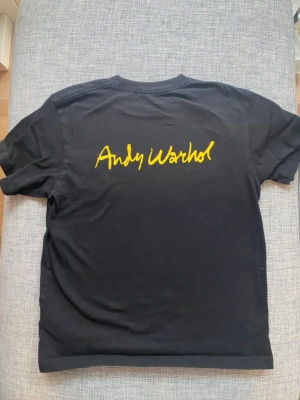 Svart Andy Warhol t-shirt XS - Svart t-shirt från Uniqlo med Andy Warhols signatur tryckt i gult på ryggen och en liten banan på bröstfickan. Klassisk passform, material bomull. Storlek XS. 