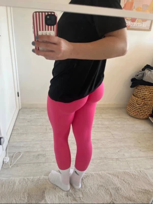 Knallrosa leggings med hög midja - Säljer ett par knallrosa leggings med hög midja och tight passform. Perfekta för dig som gillar att sticka ut och vill ha något bekvämt till träning eller chill. Materialet är stretchigt och följsamt, vilket ger en snygg siluett och bra rörelsefrihet.