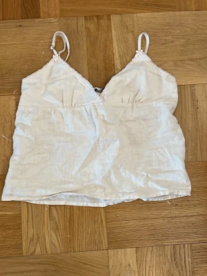 Beige  linnetopp med knytband - Söt beige linnetopp med smala axelband och v-ringning. Toppen har ett dekorativt knytband i ryggen och är tillverkad i ett lätt och luftigt linnematerial. Använd 1 gång!! Sitter som en xxs-xs