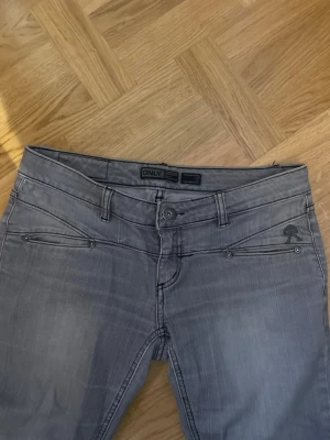 Grå vintage lågmidjade jeans från ONLY - Säljer ett par grå jeans från ONLY Limitless Denim med snygga detaljerade sömmar och unika fickor både fram och bak. Jeansen har normal passform och klassisk knappgylf. Perfekta till en chill vardagslook. Dom är vintage lågmidjade och jeansen liknar LTBs jeans i benen.