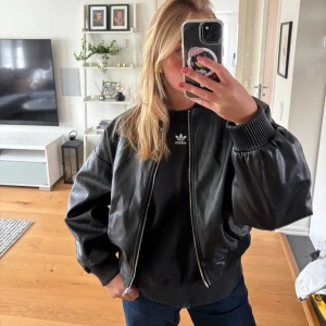 Svart skinnjacka från Zara - Snygg svart skinnjacka från Zara med ribbade muddar vid ärmslut och nederkant. Jackan har dragkedja framtill, två fickor med knapp och en klassisk rund krage. Storlek M