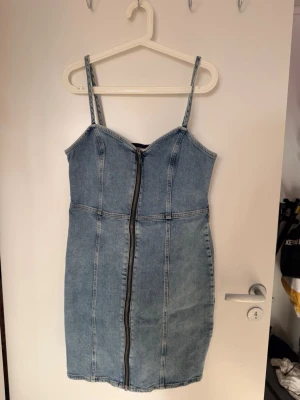 NY Jeansklänning från River Island i storlek 16.  - Jeansklänning från River Island i storlek 16. Figurnära modell med dragkedja framtill och smala axelband. Stretchig denim som sitter snyggt på kroppen. Perfekt till sommar och fest. Fint skick.  Storlek: 16 (L/XL) 