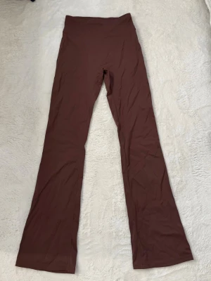 Bruna tränings leggings - Säljer ett par bruna leggings med bootcut-modell och hög midja. De är stretchiga och sitter skönt mot kroppen, perfekta för en avslappnad och trendig look. Materialet känns mjukt och följsamt, och färgen är en djup brun ton.