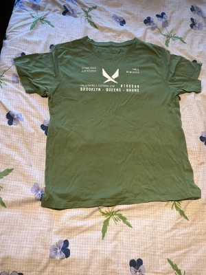 Grön t-shirt med tryck Brooklyn - Snygg grön t-shirt med vitt tryck framtill där det står 'Brooklyn - Queens - Bronx' och en grafisk logga. T-shirten har rund hals och korta ärmar, perfekt för en avslappnad streetwear-look. Tillverkad i mjuk bomull för skön känsla.