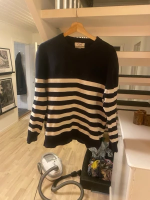 Randig stickad tröja från COS - Snygg stickad tröja från COS i marinblått och vitt med breda horisontella ränder. Tröjan har rund halsringning, långa ärmar och ribbade muddar. Perfekt för en avslappnad och trendig look.