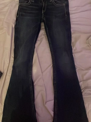 Bootcut jeans med broderade fickor - Mörkblå bootcut jeans med snygga kontrastsömmar och broderade bakfickor. Jeansen har låg midja och klassisk femficksdesign. Perfekta för dig som gillar en retro vibe och vill sticka ut lite extra. Materialet är denim med stretch för skön passform.