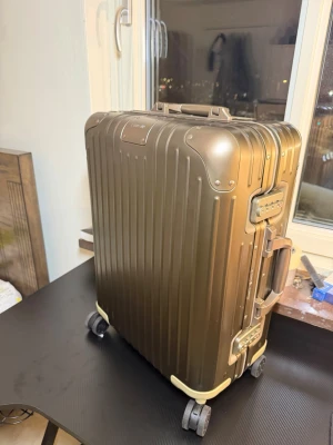 Olivgrön resväska från Rimowa - Snygg olivgrön resväska från Rimowa i aluminium med räfflad yta och robusta hörn. Väskan har fyra hjul, två handtag och integrerade TSA-lås. Perfekt för dig som vill resa med stil och kvalitet.