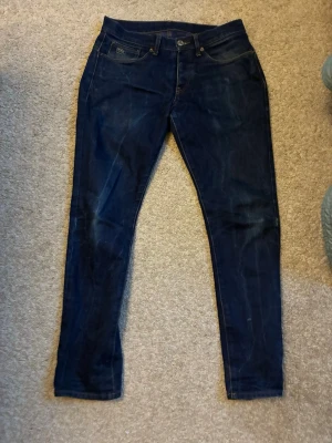 Mörkblå slim fit jeans från G-Star - Snygga mörkblå jeans från G-Star i slim fit-modell. Klassisk femficksdesign med subtila slitningar och kontrastsömmar. Jeansen har normal midja och är tillverkade i ett stretchigt denimtyg för extra komfort.