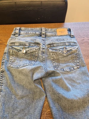 Ljusblå bootcut jeans Perfect Jeans gina tricot - Säljer ett par ljusblå jeans bootcut från ginatricor med snygga detaljerade bakfickor med knappar. Jeansen har normal midja i strl 32, men passar 32/34. Helt nya, köpte igår för 499kr och endaste provade. Säljer då jag inte vet om jag tycker om de, därav billigt pris😊