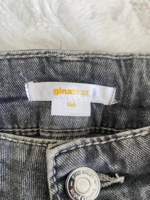 Grå bootcut jeans från Gina Tricot - Snygga grå jeans från Gina Tricot i storlek 146. Modellen har bootcut-ben och klassisk femficksdesign. Jeansen är tillverkade i denim och har en cool, tvättad look med silverfärgad knapp framtill.