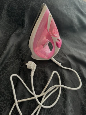Rosa strykjärn från Philips - Strykjärn från Philips i modellen EasySpeed med vit och rosa plastdesign. Har genomskinlig vattentank, ångfunktion och lång vit sladd med stickkontakt. Perfekt för att få kläder släta och snygga.