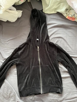 Svart velourhoodie från 157 - Svart hoodie i mjuk velour från 157 med dragkedja framtill och stor ficka på magen. Klassisk huva och ribbade muddar vid ärmslut och nederkant. Perfekt för en chill och avslappnad stil.
