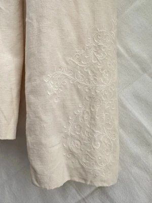 Krämvit tunn linne kavaj med broderi  - Så söt linne kavaj med  brodderi mönster på ärmarna. Kavajen har en enkel knäppning framtill. Säljer då den tyvärr inte kommer till användning. 45% linne 55% silk inner lager polyester. Stolek UK 10 men jag skulle säga att den passar strlk XXS-Xs