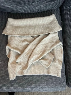 Beige off-shoulder tröja - Säljer en beige off-shoulder tröja med ribbade muddar. Tröjan är stickad och har en klassisk, enkel design som passar perfekt till kyliga dagar. Perfekt att styla med jeans eller kjol för en chill look. Säljer pågrund av att den ej kommer till användning.