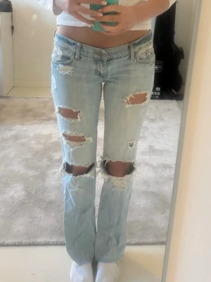 Ljusblå slitna bootcut jeans hollister - Säljer efteetraktade ljusblå bootcut jeans med slitningar och låg midja. Passar mig som har W25 L32, men skulle säga att de är w26/l30-32. Är 165cm lång