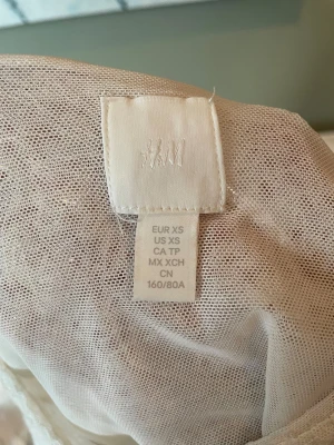 Glittrig vit topp från H&M XS - Snygg glittrig vit topp från H&M i storlek XS. Tunt och lätt material med glittriga detaljer som ger en festlig känsla. Perfekt att styla med jeans eller kjol för en trendig look.