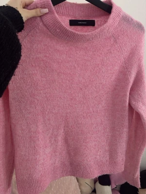 Rosa stickad tröja från Vero Moda - Mysig rosa stickad tröja från Vero Moda med rund halsringning och långa ärmar. Tröjan har en enkel, rak passform och ribbade muddar vid hals, ärmslut och nederkant. Perfekt för dig som gillar en söt och avslappnad stil.