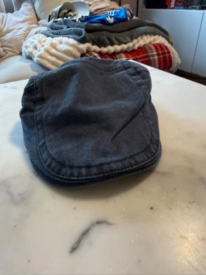 Mörkblå keps i bomull - Säljer en mörkgrå flat cap i mjukt bomullstyg. Klassisk och stilren design med rundad skärm och justerbart band bak. Perfekt för dig som vill ha en tidlös och avslappnad look.