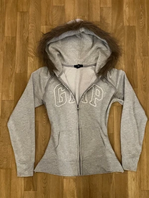 Grå GAP zip med päls - Pälsen är påsydd av mig precis som midjan är sydd för att ha en tightare passform, därför tvätta den helst för hand. Själva hoodien är köpt secondhand så det kan finns små skavanker men inget som är direkt märkbart isf. Finns även uppe på min vinted, skicka ett dm för fler frågor eller bilder. Kolla mina andra annonser för likande produkter!