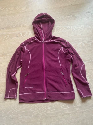 Magentalila hoodie från Norrøna - Magentalila hoodie från Norrøna med dragkedja framtill och två fickor med dragkedja. Snygga kontrastsömmar i vitt och huva för extra komfort. Tillverkad i mjukt fleecematerial, perfekt för chill dagar eller lager på lager. Warm 1