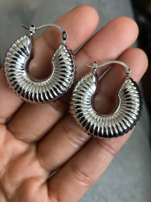s925 sterling Silvriga räfflade hoops örhängen - Säljer ett par chunky hoops i silverfärgad metall med räfflad yta och halvmåneform. Örhängena har en cool retrovibe och stängs med klassisk bygel. Perfekta för dig som vill sticka ut lite extra med accessoarerna. material: sterling silver pläterat s925 stamped