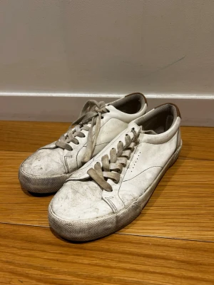 Bershka sneakers *39* - Klassiska vita sneakers i lågt snitt med beige detaljer på hälen och matchande vita snören. Tillverkade i slätt läder med diskreta sömmar och perforeringar på sidan för ventilation. Perfekta för en clean och stilren look.