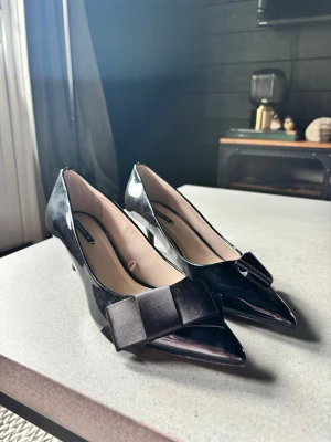 Svarta klackskor Zara  - Snygga klackskor  i lack med spetsig tå och dekorativ rosett framtill. Sååååå fina 💗💗💗aldrig använda 