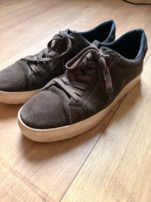 Bruna Vagabond - Snygga bruna Vagabonds i mocka med klassisk låg profil och vita sulor. Skorna har matchande bruna skosnören och en enkel, stilren design som passar till det mesta. Perfekta för dig som gillar en clean och avslappnad look.