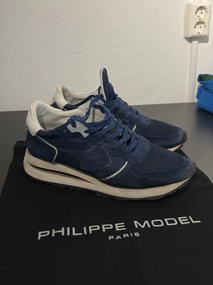 Blå Philippe Model sneakers - Snygga sneakers från Philippe Model i marinblå mocka och mesh med vita detaljer och vit sula. Klassisk låg modell med logga på sidan och på plösen. Skorna har blå skosnören och en sportig vibe som passar till många olika stilar.