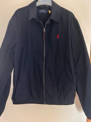 Marinblå vindjacka från Polo Ralph Lauren - Det är en tunnare jacka för våren i storlek M, inga slitningar alls på jackan, vid frågor är de bara att höra av sig 