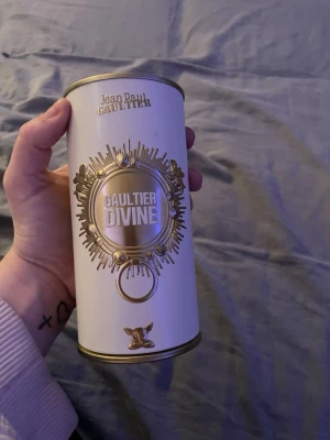 Jean Paul Gaultier Divine parfym - Snygg parfym från Jean Paul Gaultier i en vit och guldig metallburk med detaljerad design. Burken har texten 'Gaultier Divine' i mitten och eleganta gulddetaljer runt om. Perfekt för dig som gillar lyxiga och unika dofter.lite gran e använt av den men mycket kvar. 30 ml