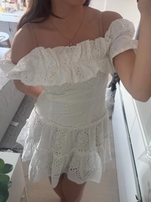 Vit offshoulder volangklänning - Superfin vit kortklänning med offshoulder och volangdetaljer. Klänningen har broderade spetsmönster och är perfekt för sommarens alla tillfällen och stundenyen. Sitter snyggt med figurnära passform och har en romantisk vibe. Från Zara i storlek L men sitter som en M/S. 