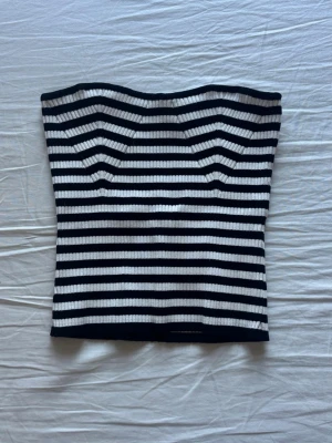 Randig tubtopp från Gina Tricot - Snygg ribbad tubtopp från Gina Tricot i svart och vitt med horisontella ränder. Toppen är axelbandslös och har en figurnära passform.
