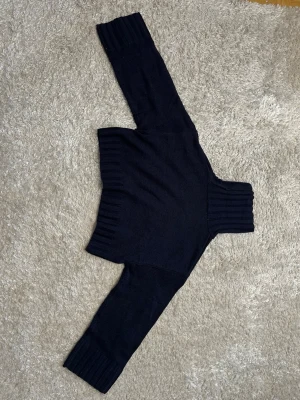 Mörkblå cropped polotröja stickad - Säljer en mörkblå stickad cropped polotröja med bred ribbad krage, muddar och nederkant. Tröjan har lång ärm och är perfekt för lager på lager. Materialet känns mjukt och stretchigt, vilket gör den både bekväm och snygg.