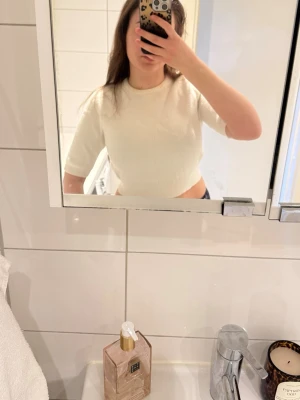 Vit croppad stickad topp från Gina Tricot - Säljer en vit croppad stickad topp från Gina Tricot med korta ärmar och rund halsringning. Perfekt för dig som gillar en enkel och clean look. Materialet är mjukt och ribbat vid hals och nederkant.