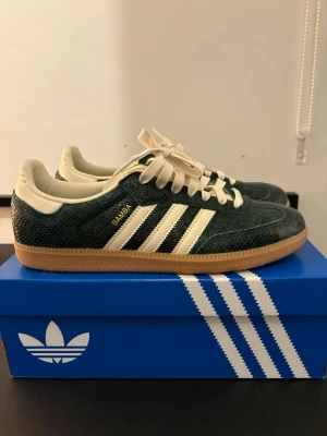 Adidas Samba gröna sneakers - Säljer ett par Adidas Samba sneakers i mörkgrönt ormskinnsmönstrat material med vita detaljer och klassiska tre ränder på sidan. Skorna är helt nya och köpa på adidas hemsida (endast testade i 2 dagar då de är för små för mig).