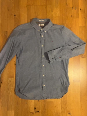 Blå skjorta från Tommy Hilfiger Denim - Klassisk blå skjorta från Tommy Hilfiger Denim med button-down krage och vita knappar. Skjortan har lång ärm och den ikoniska lilla Hilfiger-loggan broderad på bröstet. Regular fit och tillverkad i mjuk bomull för en clean och stilren look.