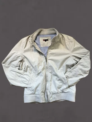 Beige jacka från dressman - Snygg beige jacka från dressman med dragkedja framtill, ribbade muddar och ståkrage. Jackan har två sidofickor och en diskret logga på insidan. Perfekt för alla dagar och enkel att matcha med olika outfits.