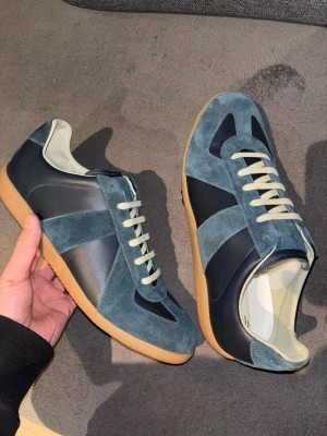 Maison Margielas gats - Stilrena mörkblå sneakers från Maison Margiela med ovandel i mocka och skinn, beige innersula och vita snören. Klassisk siluett med gummisula och diskreta detaljer som ger en exklusiv känsla. Perfekta för dig som gillar minimalistisk design. Allt og ingår samt orderbevis bilder från goat.  Storlek 44, Ställ frågor!!