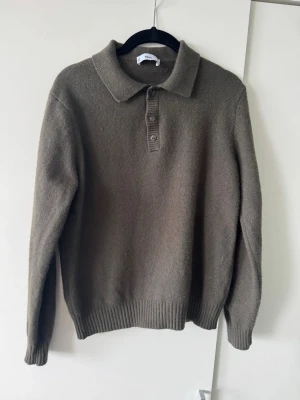 Olivgrön stickad polotröja - Snygg olivgrön stickad tröja med krage och tre knappar framtill. Tröjan har långa ärmar och ribbade muddar vid ärmslut och nederkant. Perfekt för dig som gillar en stilren och avslappnad look.
