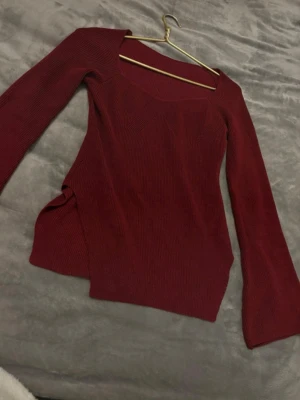 Vinröd ribbad topp med lång ärm - Trendig vinröd topp med ribbad struktur och lång ärm. Toppen har en snygg fyrkantig ringning och är figurnära i modellen. Perfekt att styla med jeans eller kjol för en cool look.