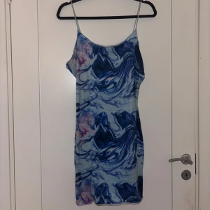 Blå mönstrad kort klänning - Säljer en kort klänning med tunna axelband och ett unikt blått marmorerat mönster. Klänningen har en figurnära passform och är perfekt för sommardagar. Materialet känns lätt och svalt mot huden.