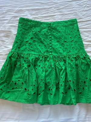 Grön volangkjol med knappar - Säljer en grön kortkjol i bomull med broderade hålmönster och volang nedtill. Från Zara. Den har tappat en knapp som syns på bilderna. Det är inget som syns när man har den på sig 