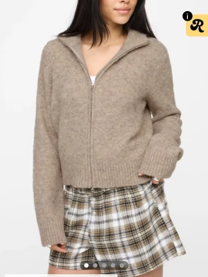 Beige ziptröja i mjuk ullmix - HELT NY ME PRISLAPP! Mysig beige tröja med dragkedja framtill och hög krage. Tillverkad i en fluffig ullmix med ribbade muddar vid ärmslut och nederkant. Perfekt för lager-på-lager och chill dagar.