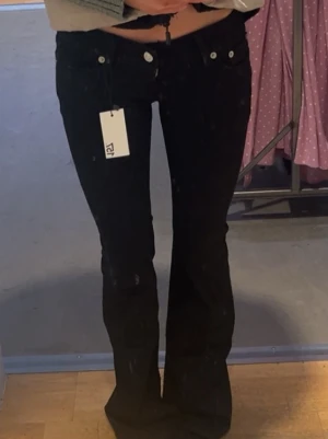 Svarta bootcut jeans från lager  - Snygga svarta bootcut jeans från lager med klassisk femficksmodell och hög midja. Jeansen har utsvängda ben och silverfärgade knappar. Perfekta för en trendig och avslappnad look.