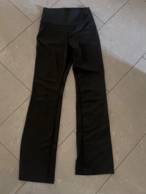 Svarta bootcut leggings - Säljer ett par svarta leggings med bootcut-modell och hög midja. De är stretchiga och sitter skönt på kroppen, perfekta till en avslappnad look. Materialet känns mjukt och följsamt, men exakt material är okänt. Inga synliga loggor eller märken.