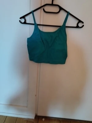 Turkos body med smala axelband - Snygg turkos body med smala axelband och enkel, rak skärning. Tillverkad i mjukt stretchigt material som sitter skönt mot kroppen. Perfekt att bära under tröjor eller som ett statement-plagg. Inga synliga detaljer eller mönster.