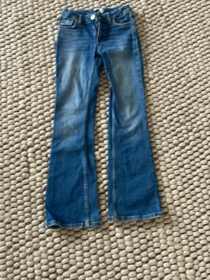 Blå bootcut jeans från Gina tricot  - Säljer ett par blå bootcut jeans med lätt slitna detaljer framtill och bakfickor. Jeansen har klassisk femficksmodell, normal midja och är tillverkade i denim. Perfekta för dig som gillar en retro och avslappnad stil.