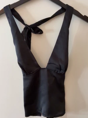 Gina tricot topp - Svart satin topp som man knyter i nacken och ryggen från Gina tricot i strl 34. Oanvänd med lapp kvar. 
