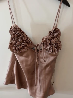 Zara topp - Supersnygg satin topp från Zara med blommor. Aldrig använd med lapp kvar. Toppen har en dragkedja i sidan och band man knyter framtill